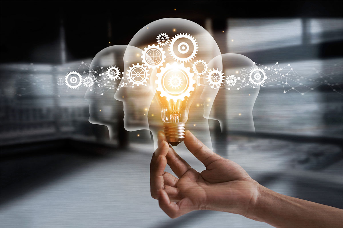 An outstretched hand holds a glowing light bulb, surrounded by abstract representations of faces and interconnected gears, symbolizing innovative ideas and creativity.