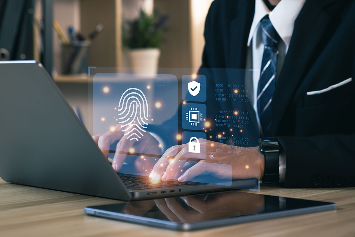 A business professional in a suit using a laptop, with a digital fingerprint and security icons displayed on the screen, suggesting biometric authentication and cybersecurity.