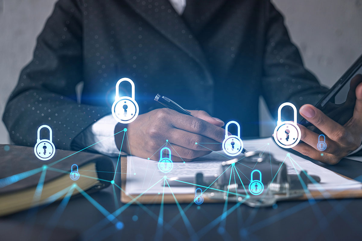 A close-up of a person's hand holding a pen, writing on a notepad, with a smartphone nearby. Digital lock icons and network lines are overlaid, symbolizing cybersecurity and data protection.